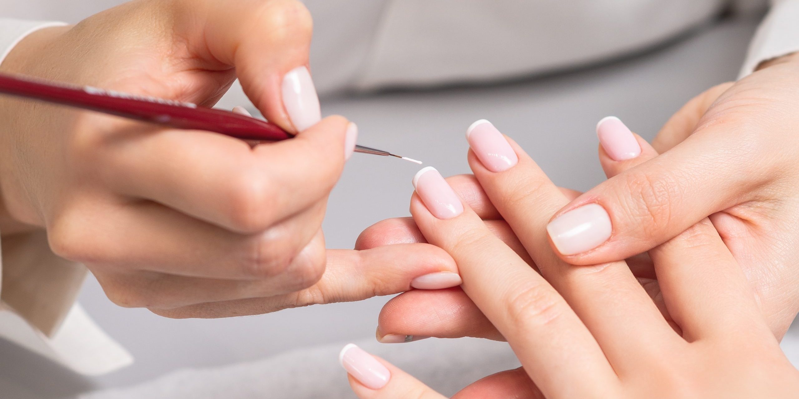 Mano de mujer joven recibiendo manicura francesa por esteticista en salón de uñas.